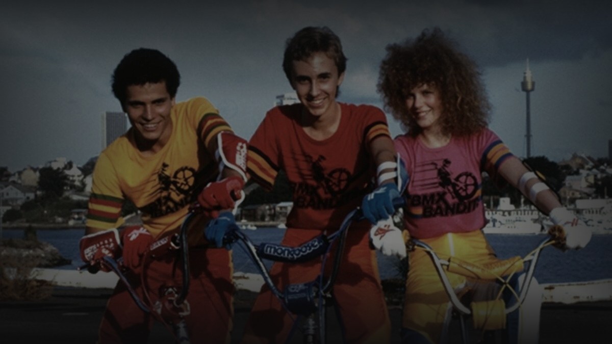 Still from BMX Bandits (1983) — 16:9 still from Letterboxd (1200x675 crop variant), baked through scripts/bake_dark_photo.py at default factor 0.45
