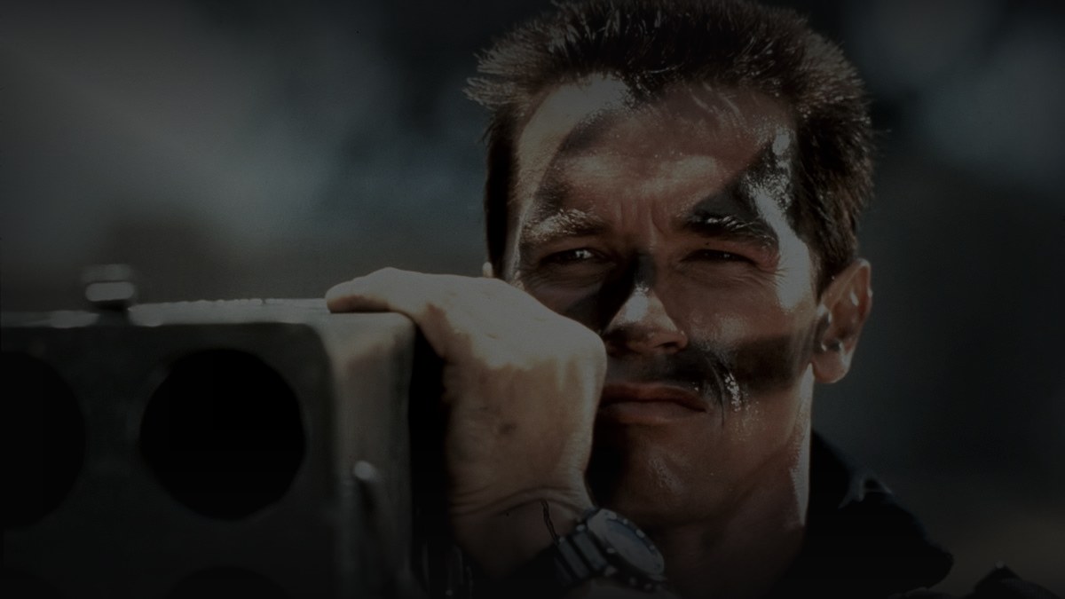 Still from Commando (1985) — 16:9 still from Letterboxd (the 1200x675 crop variant), source pre-darkened 0.80 to handle the high-key daylight source, then baked through scripts/bake_dark_photo.py at default factor 0.45, output brightness 33.8 (within the 25-35 daylight target)