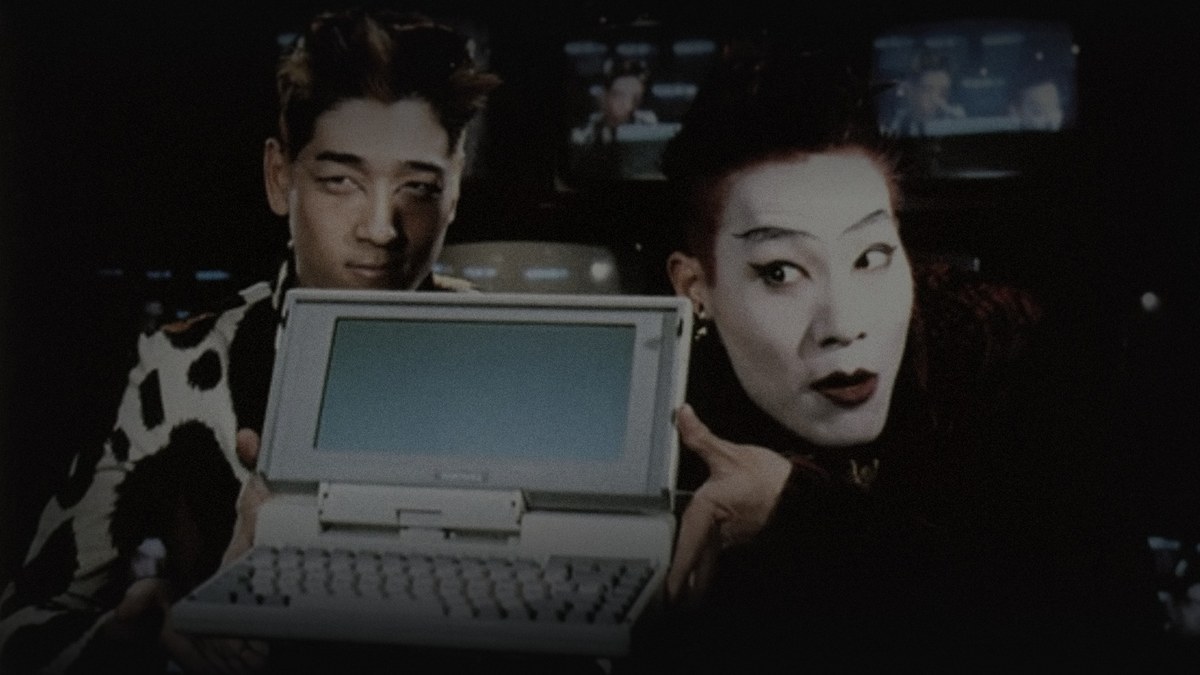 Still from Hackers (1995) — TMDB backdrop mRtplFVP5hXFWtsoj3jlxDiqaN1.jpg, selected after checking the Letterboxd og:image and five TMDB backdrop candidates, baked through scripts/bake_dark_photo.py at factor 0.45, output brightness 32.1, downscaled to 1200x675